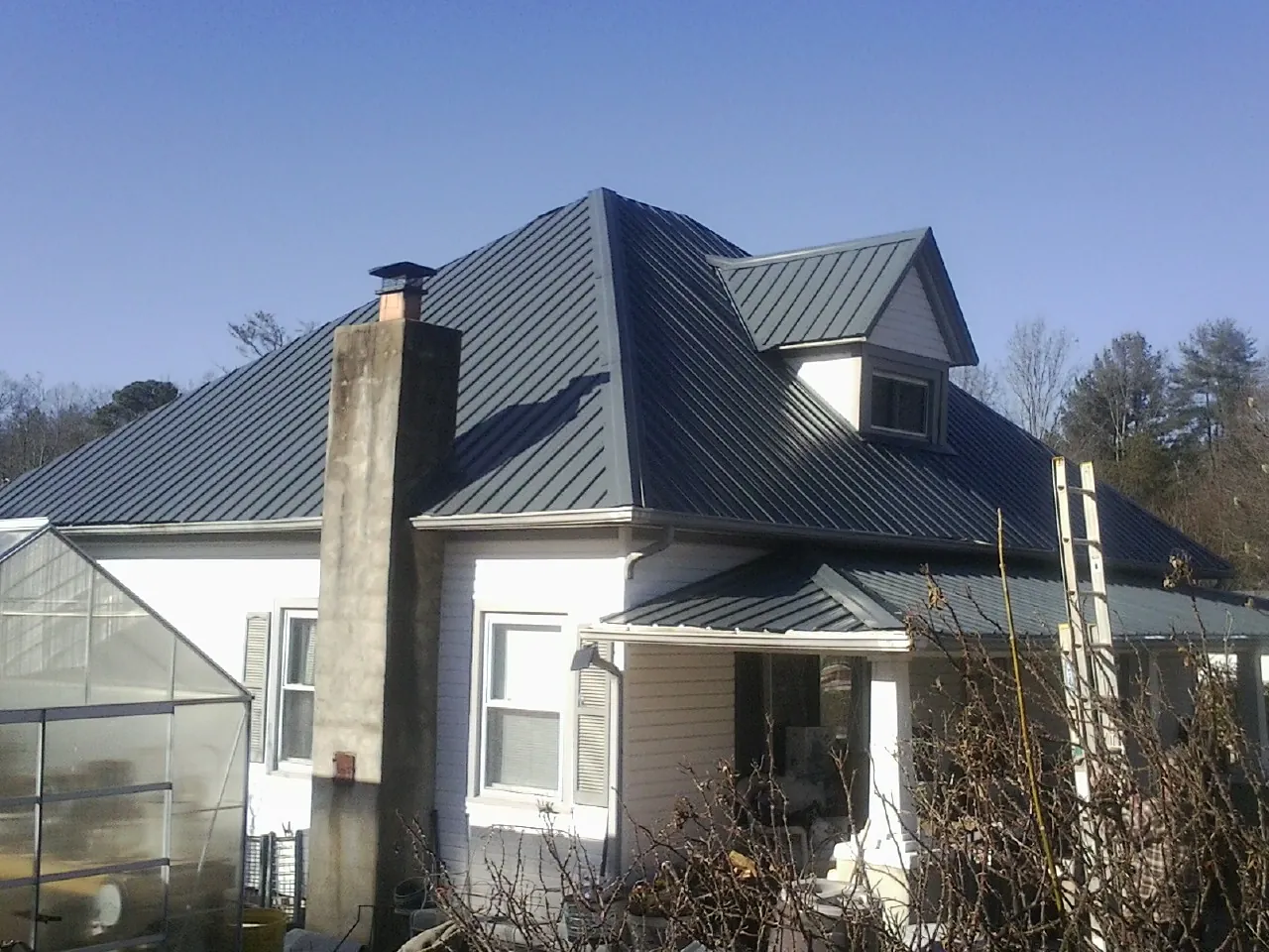 Dark blue standing seam metal roof on a white farmhouse with dormer — Slate & Tile Roof Repair by Roofing Brothers in Eldorado Springs