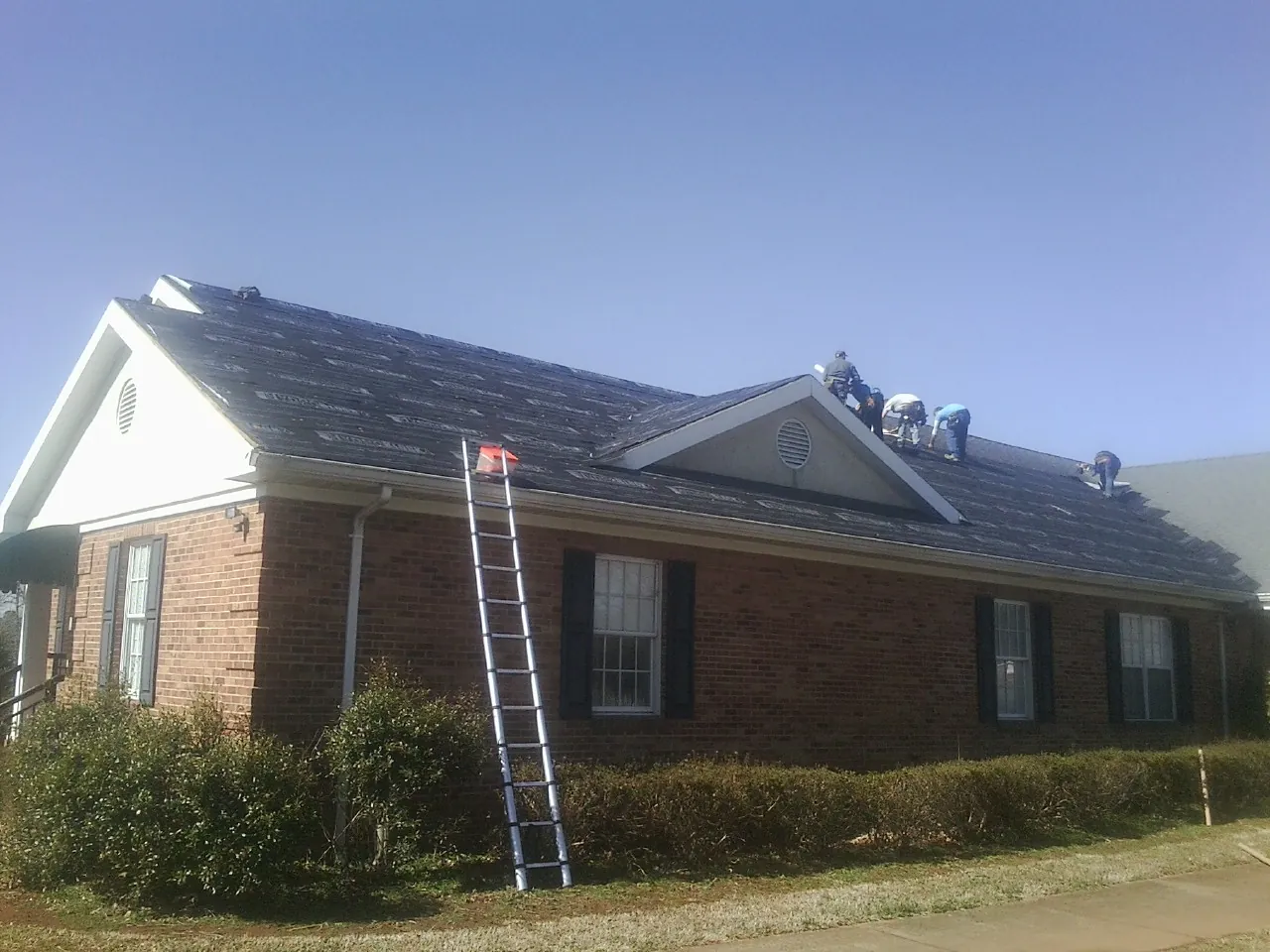 Crew tearing shingles off a brick ranch roof with a ladder set — Emergency Roof Repair work by our crew in Eldorado Springs