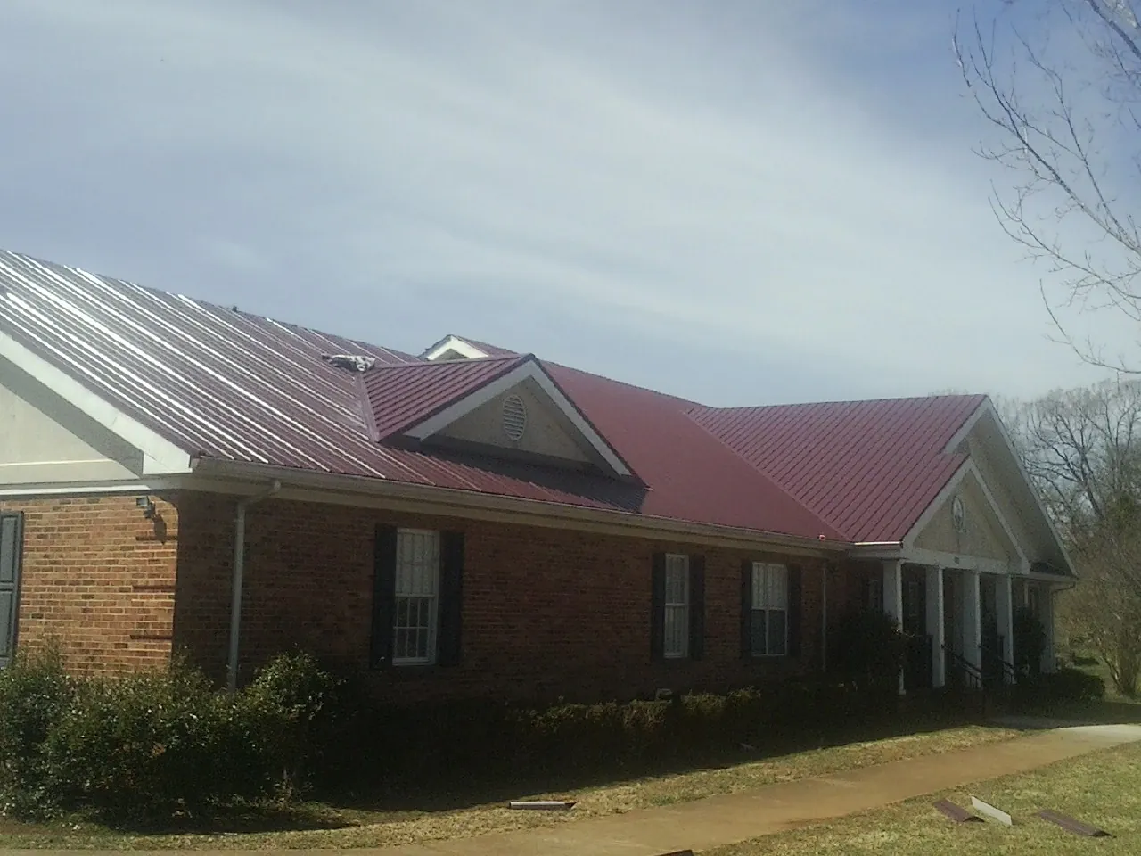 Red metal roof with gabled entries on a long brick building, from a Hail Damage Roof Repair job in Eldorado Springs