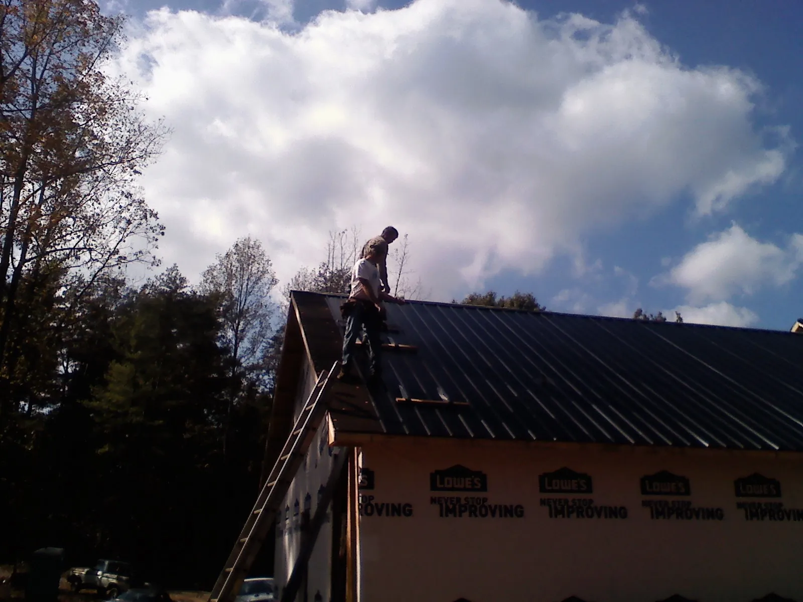 Roofer fastening dark metal panels high against a cloudy sky, from a Roof Inspection job in Eldorado Springs