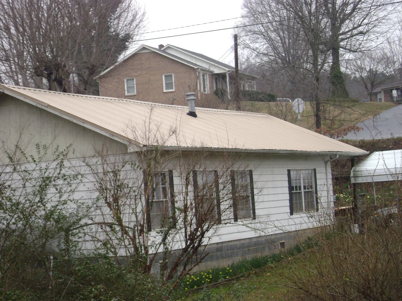 Tan metal roof on a white sided house set into a hillside — Commercial Roofing by Roofing Brothers in Eldorado Springs